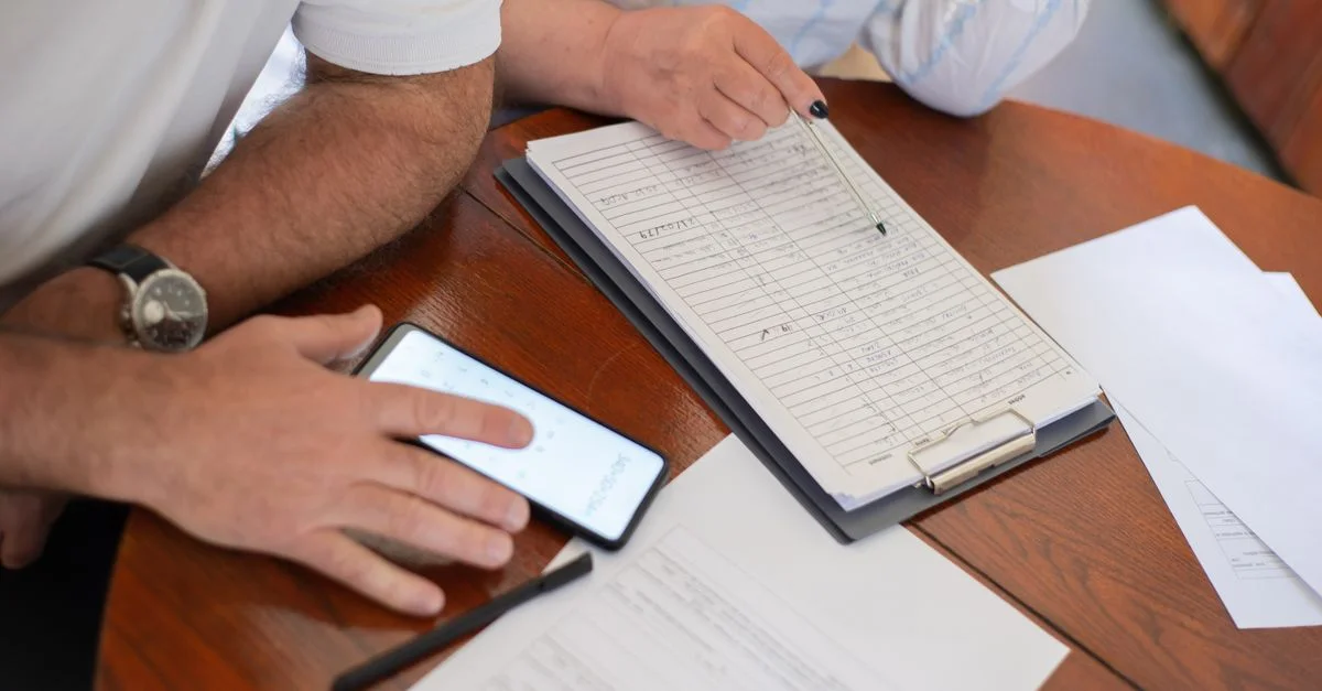 Couple senior examinant des factures et des documents avec un smartphone et un bloc-notes à la maison.