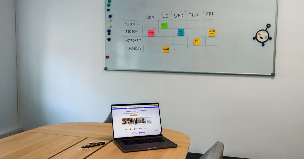 Configuration de bureau avec une table de conférence, un ordinateur portable et un calendrier sur tableau blanc organisé, mettant en avant un espace de travail axé sur la technologie.