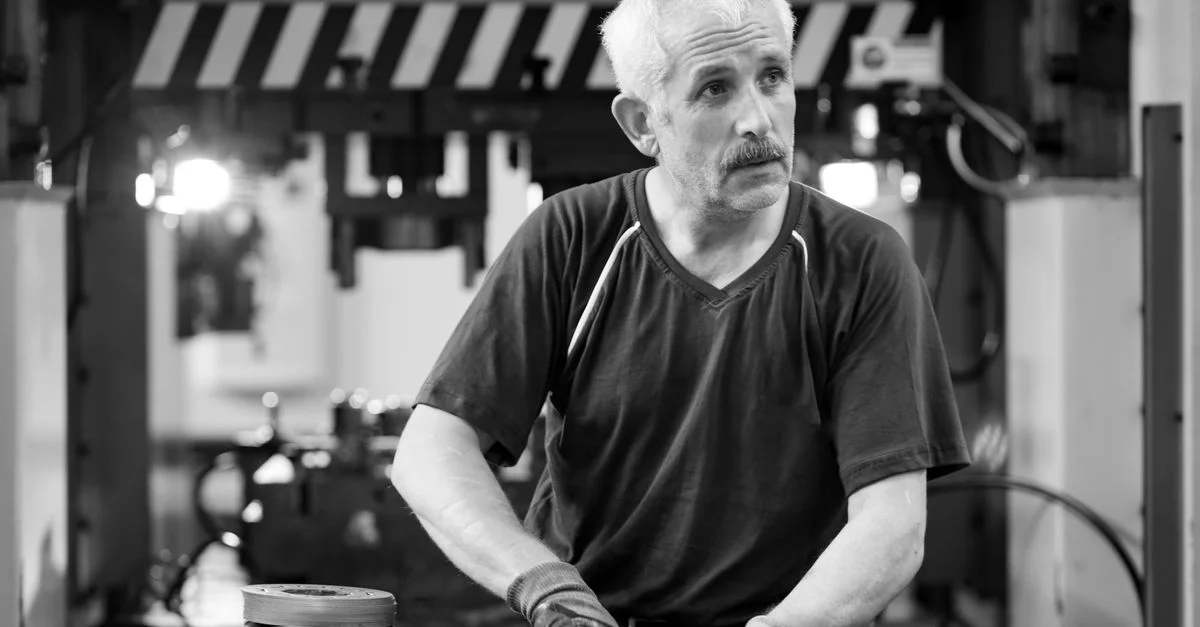 Photo en noir et blanc d'un travailleur âgé avec des gants dans un atelier.