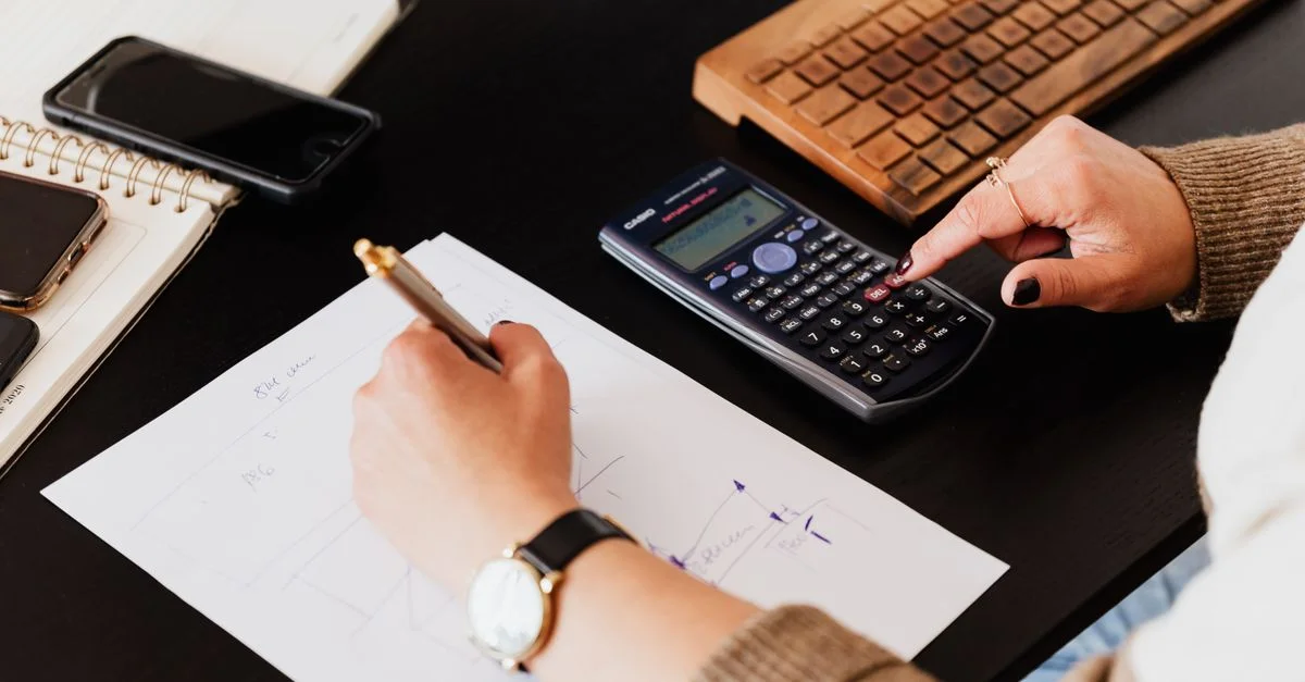 Gros plan sur des mains utilisant une calculatrice et un carnet sur un bureau, analysant des documents.