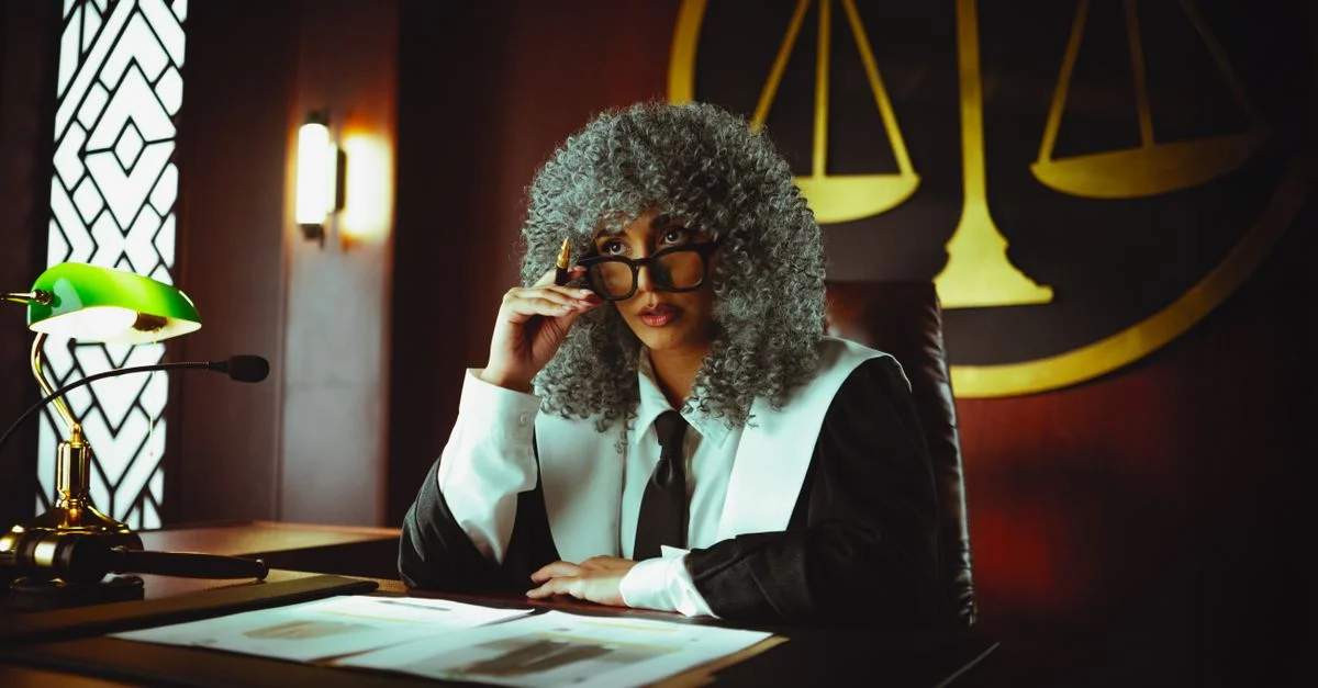 Juge en tenue traditionnelle assis à un bureau de tribunal avec une expression sérieuse.