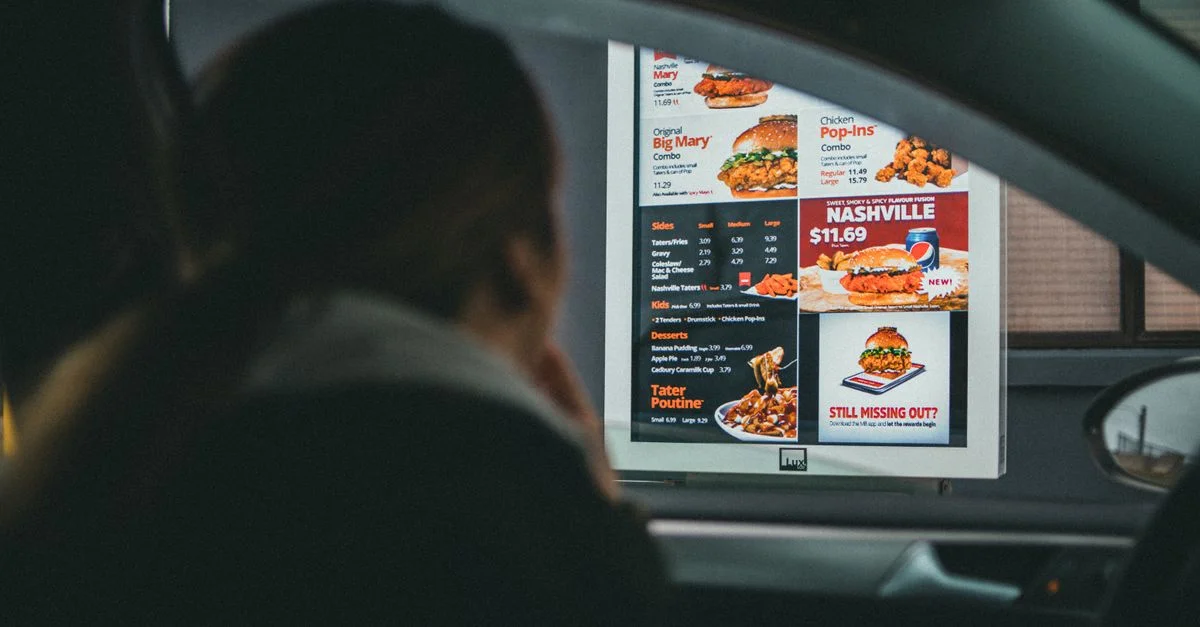 Une femme dans une voiture consulte le menu au drive-in d'un fast-food, prête à commander son repas.