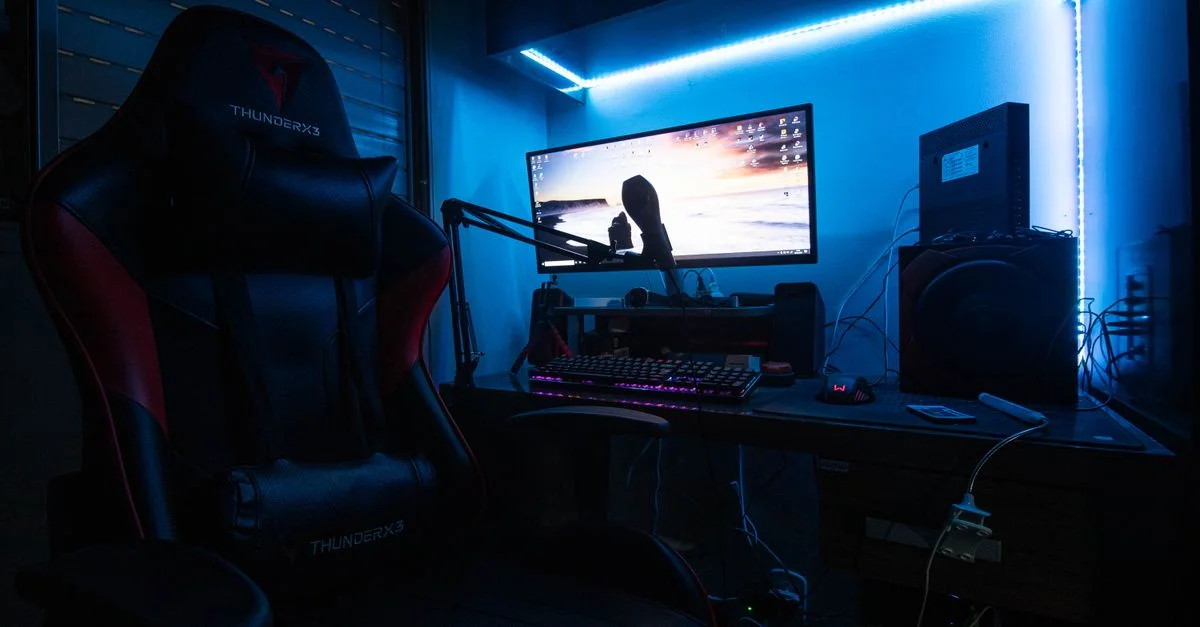 Un bureau de gaming élégant avec un moniteur, une chaise de gaming, et des lumières LED créant une ambiance immersive.