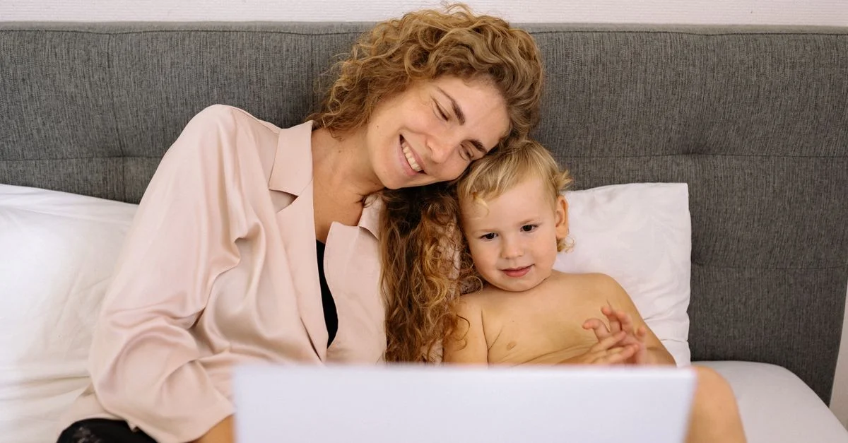 Mère et enfant souriant en regardant quelque chose sur un ordinateur portable ensemble au lit, profitant d'un moment de qualité.