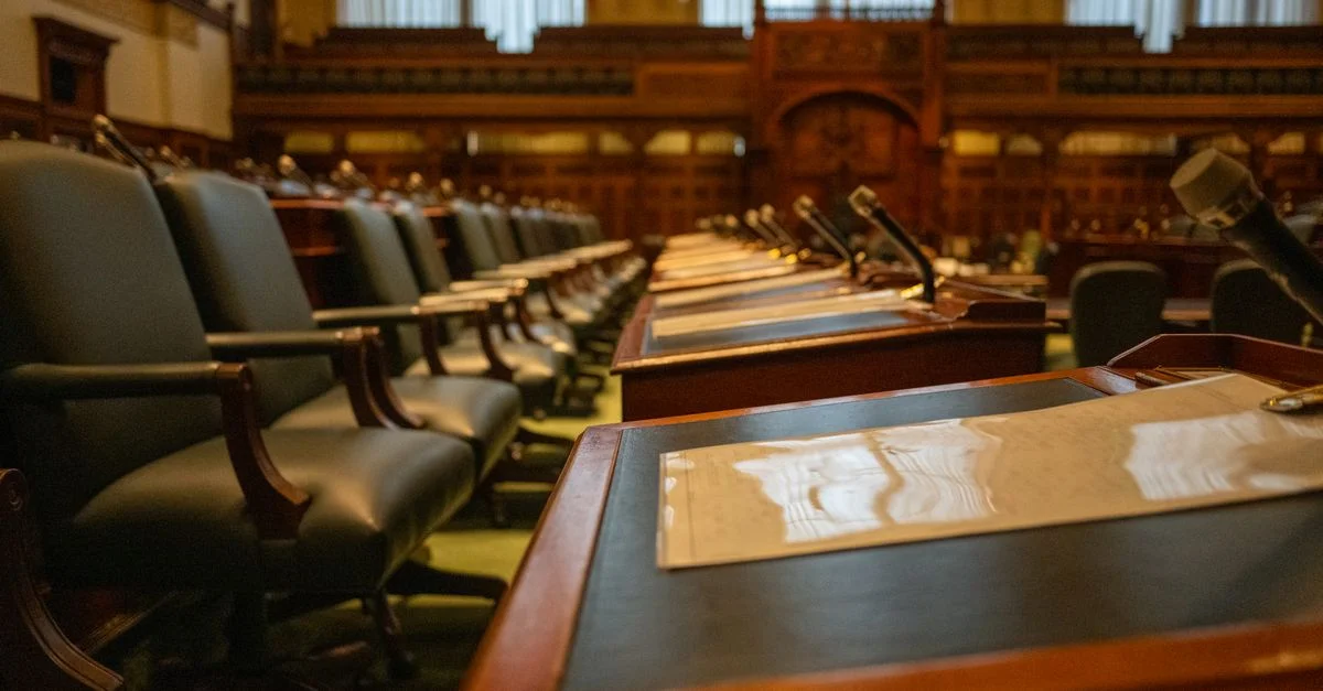 Vue détaillée d'une chambre législative vide avec des rangées de bureaux et de microphones, évoquant la gouvernance.