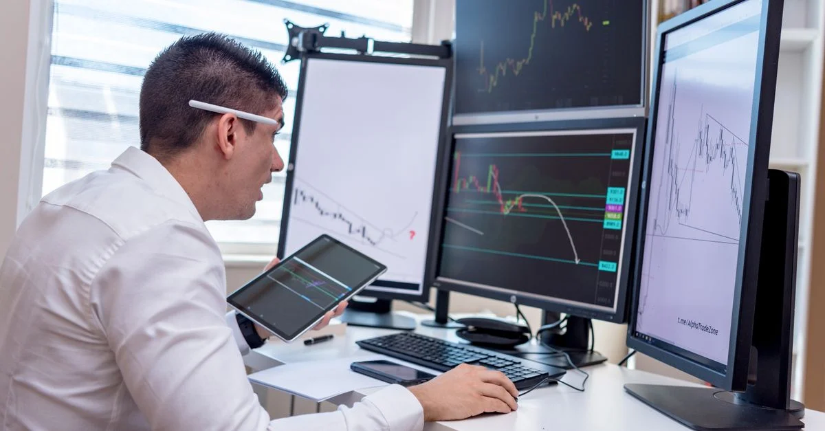 Un homme analysant des graphiques du marché boursier sur plusieurs écrans à un poste de travail.