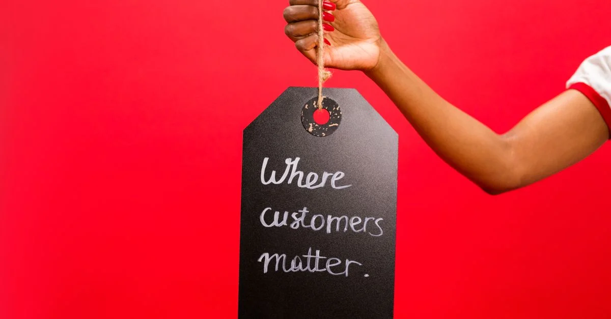 Une main tenant une étiquette avec le texte 'Où les clients comptent' sur un arrière-plan rouge vif, soulignant le service client.