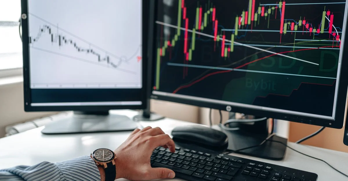 Un homme d'affaires utilisant des écrans doubles pour analyser les tendances du marché boursier avec des tableaux et des graphiques.