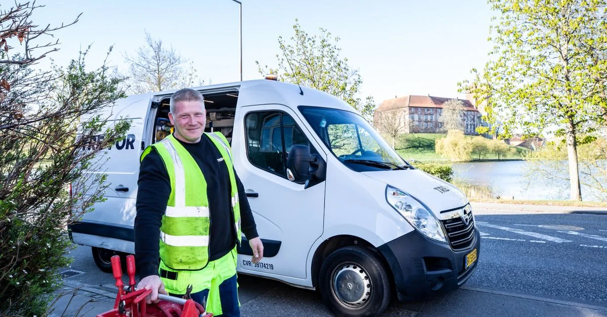 Travailleur souriant en gilet réfléchissant se tenant à côté d'un fourgon avec des outils.