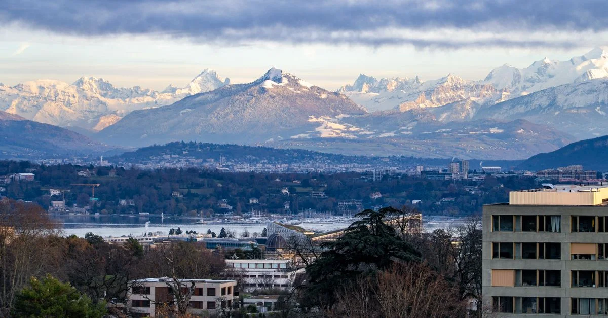 Une vue imprenable sur Genève avec les Alpes suisses en arrière-plan, sous un ciel nuageux en journée.