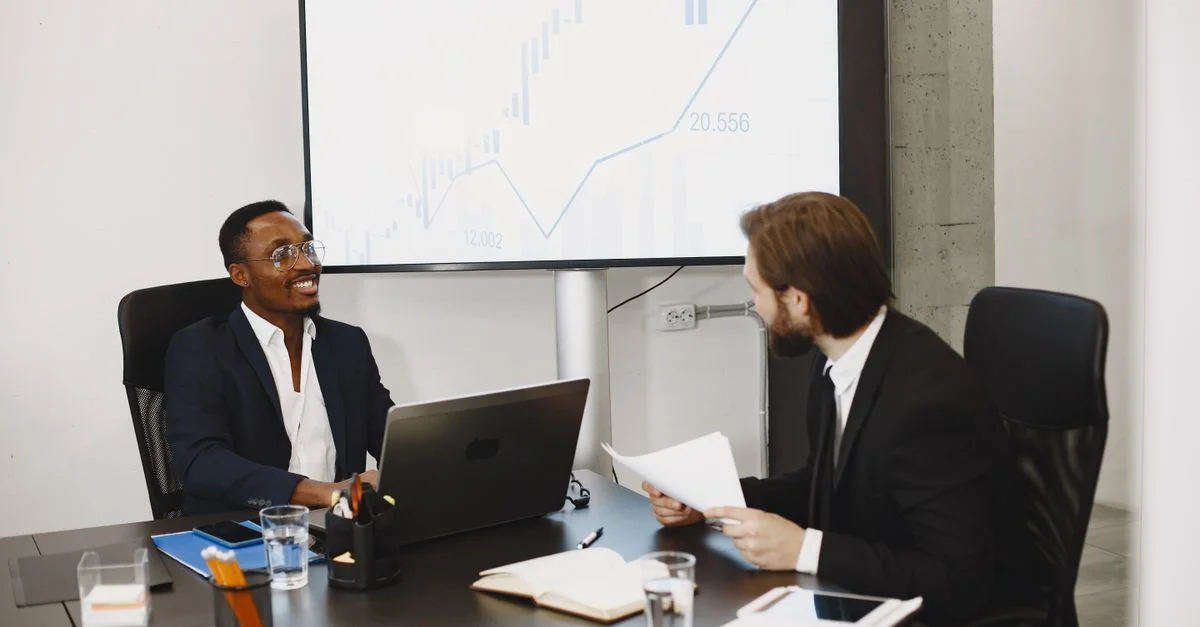 Deux hommes d'affaires lors d'une réunion professionnelle discutent des données sur un grand écran dans un bureau moderne.