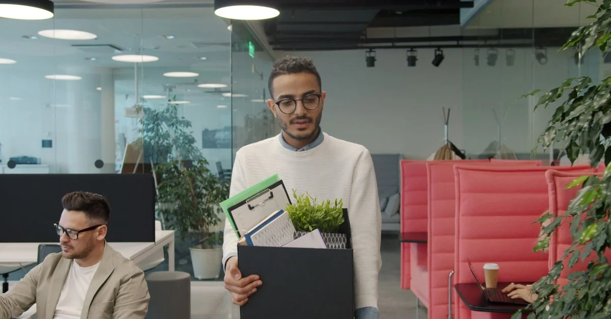 Un homme d'affaires quitte son bureau avec ses effets personnels dans un carton, symbolisant un changement d'emploi ou une démission.