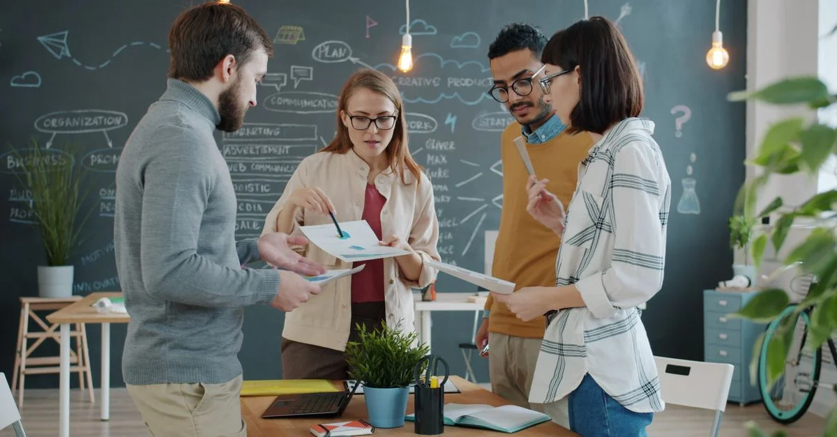 Quatre professionnels se livrent à une séance de brainstorming créative dans un bureau moderne équipé d'un tableau noir.