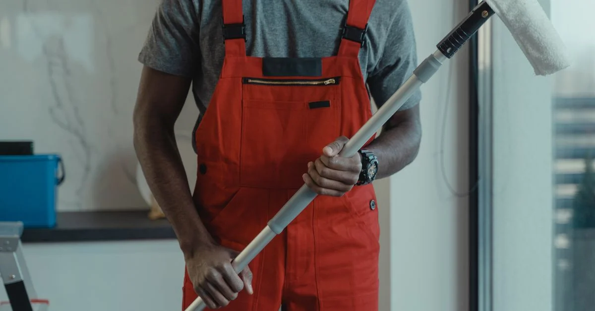 Un nettoyeur professionnel portant une salopette rouge tient une serpillère tout en nettoyant à l'intérieur.