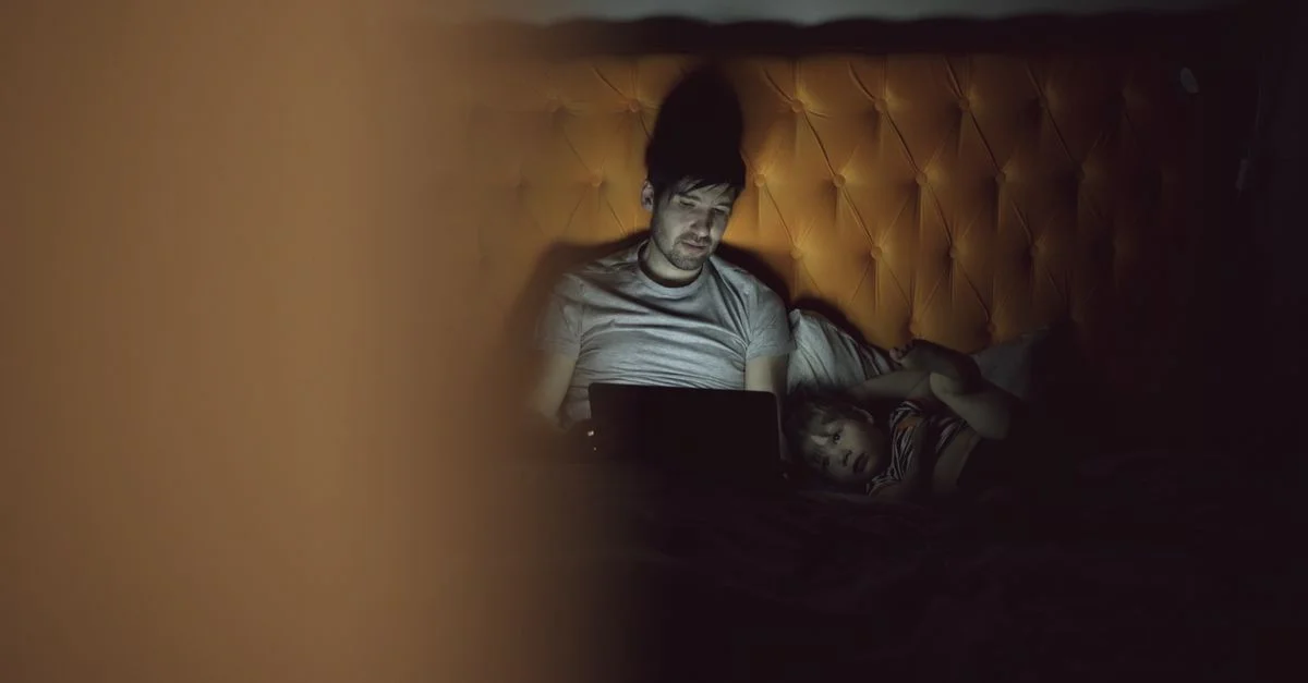 Un père et son enfant passant du temps le soir au lit en utilisant un ordinateur portable, créant une atmosphère chaleureuse.