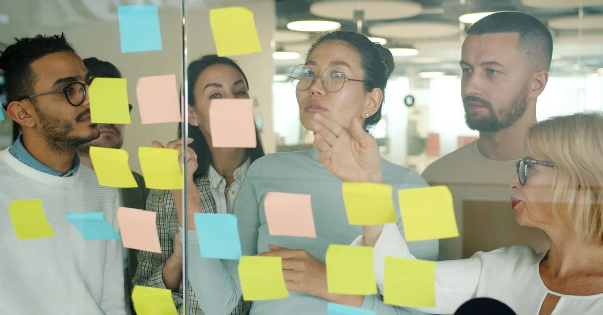 Un groupe d'adultes aux profils variés, en pleine séance de brainstorming avec des post-it dans un bureau moderne.