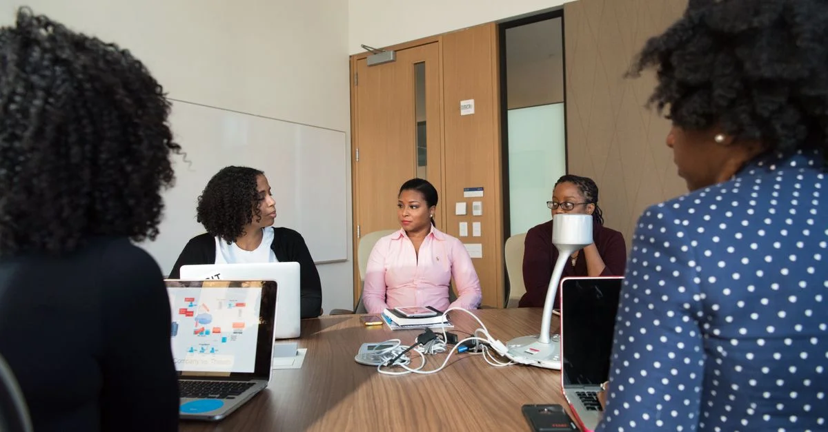 Équipe diversifiée d'adultes collaborant dans une salle de réunion avec des ordinateurs portables et des documents sur la table.