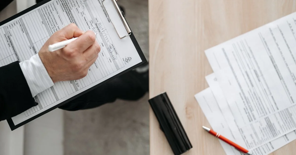 Vue en plongée d'une personne remplissant des formulaires sur un clipboard, mettant l'accent sur le travail administratif et la documentation.