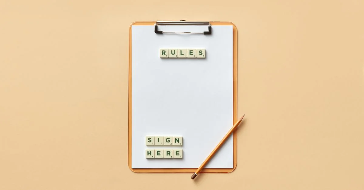 Vue de dessus d'un clipboard avec des lettres en carrelage écrivant 'règles' et 'signez ici', accompagné d'un crayon sur un fond beige.
