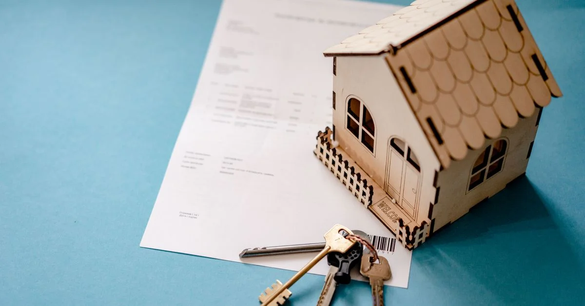 Maison miniature en bois avec clés et contrat symbolisant les transactions immobilières.