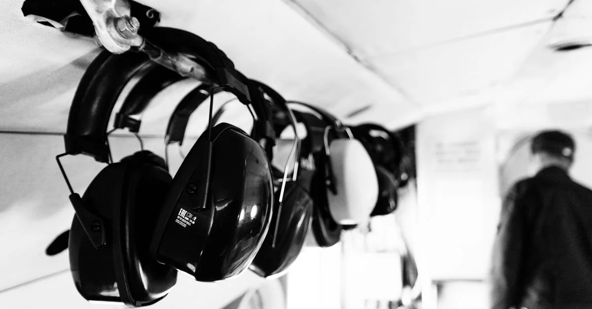 Photo monochrome d'un casque audio suspendu à l'intérieur d'un avion, avec une personne en arrière-plan.