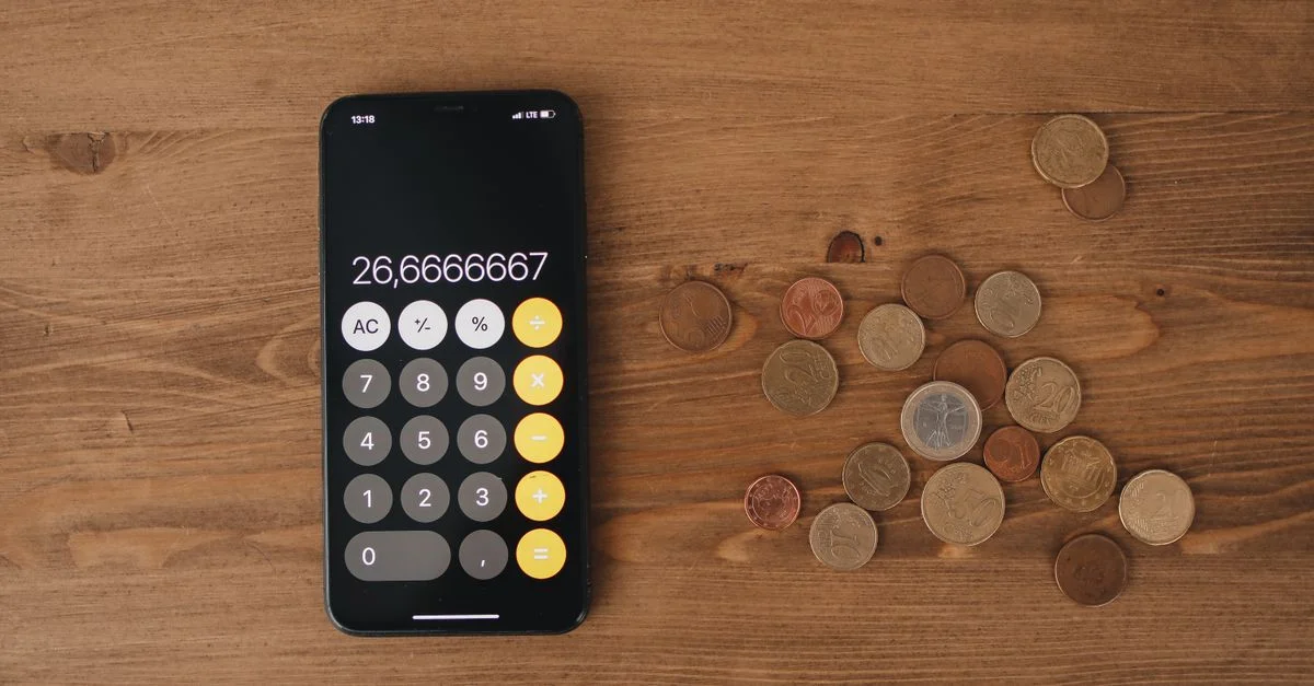 Vue de dessus d'une calculatrice smartphone avec des pièces de monnaie européennes sur une surface en bois, symbolisant la finance moderne.