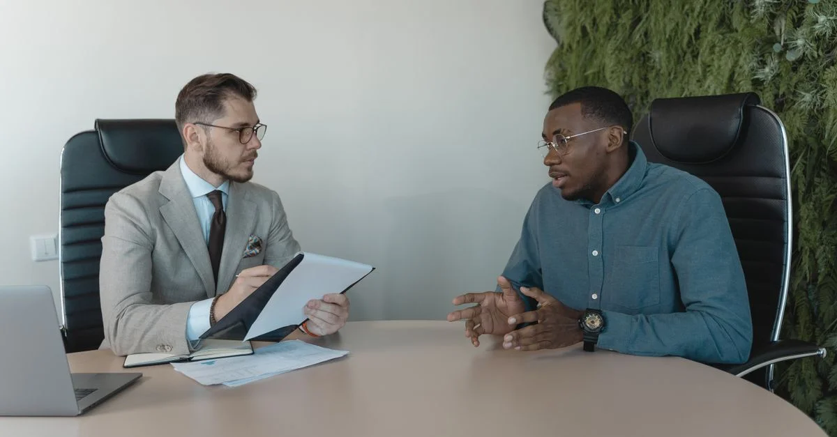 Deux hommes d'affaires engagés dans une discussion lors d'un entretien d'embauche dans un environnement de bureau contemporain.