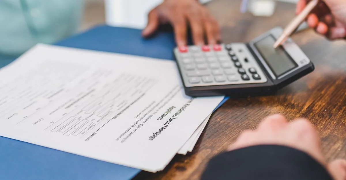 Mains utilisant une calculatrice avec des documents immobiliers sur un bureau, indiquant une transaction financière ou une réunion.