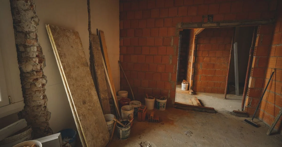 Un mur en briques rouges en construction avec des outils et des matériaux éparpillés autour dans un projet de rénovation.
