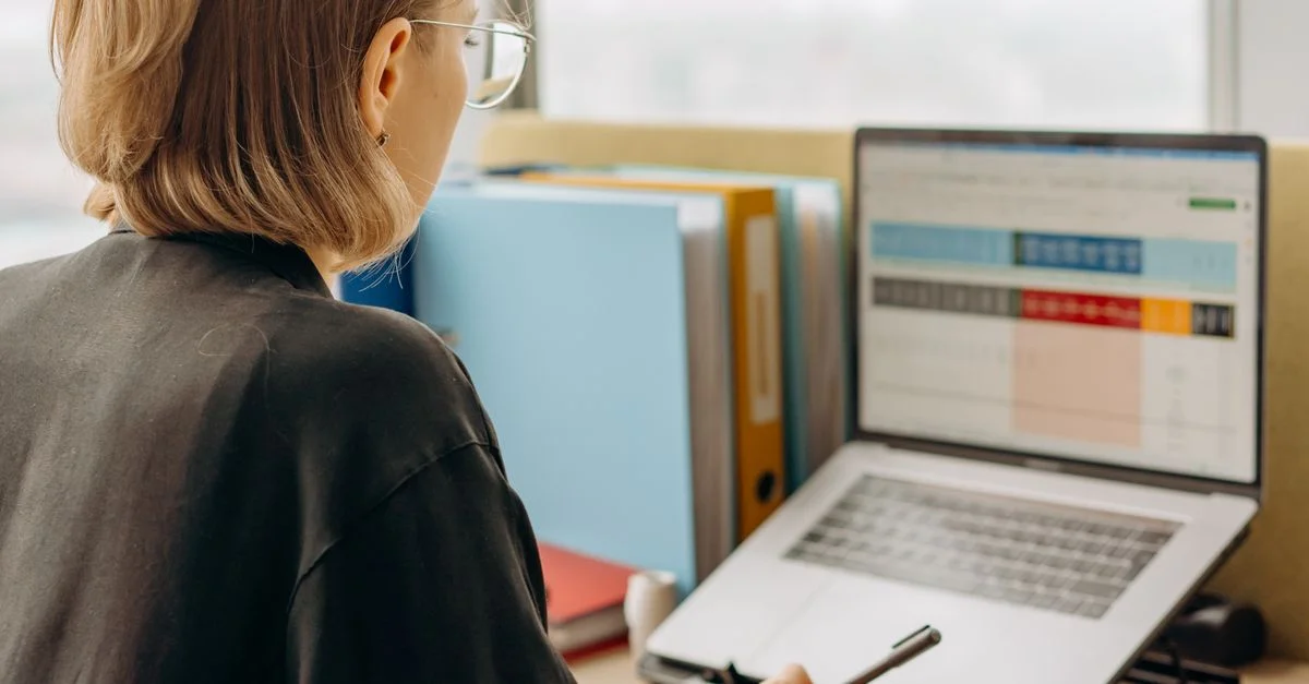 Femme professionnelle examinant des données sur un ordinateur portable, travaillant dans un environnement de bureau moderne.