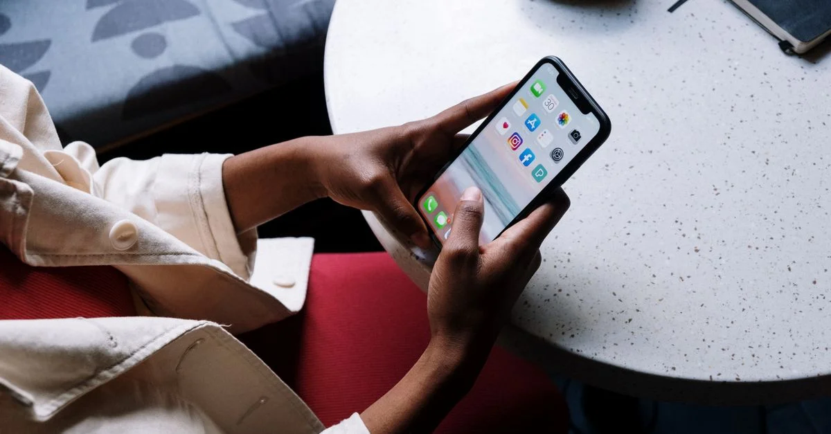 Une personne consulte des applications de réseaux sociaux sur un smartphone en étant assise à une table de café.