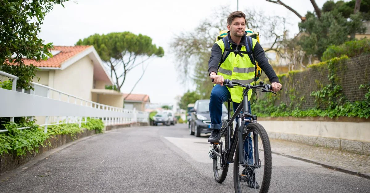 Un coursier masculin à vélo sur une rue calme au Portugal, portant un gilet réfléchissant.
